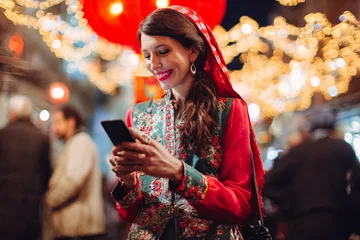 A cheerful woman in traditional clothing using her smartphone during a festive moment, showing how easily the CD334 app fits into everyday life.